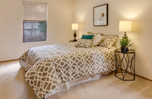 New cream colored carpet in master bedroom with queen size bed and decorative shams.