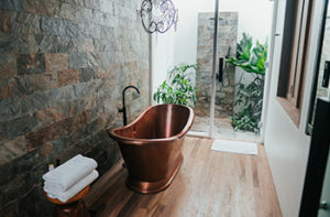 Wood look laminate floors in a spa-like bath with a antique brass tub and stone walls.