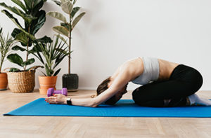 A woman practices yoga on a blue mat in a serene setting with plants and light-colored vinyl flooring