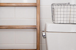 White porcelian tile walls are featured in a small bathroom with a basket of towels.