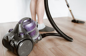 Woman is vacuuming her vinyl flooring using a purple handheld vacuum