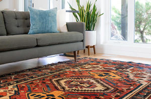 A brightly colored area rug is placed in the living room near a gray couch adding fo a chic bohemian look