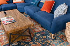 A brightly colored silk Oriental rug lays under a blue couch and rustic wood coffee table.