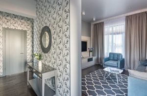 A grey door opens to two beautifully designed rooms that are divided by a wallpapered wall.