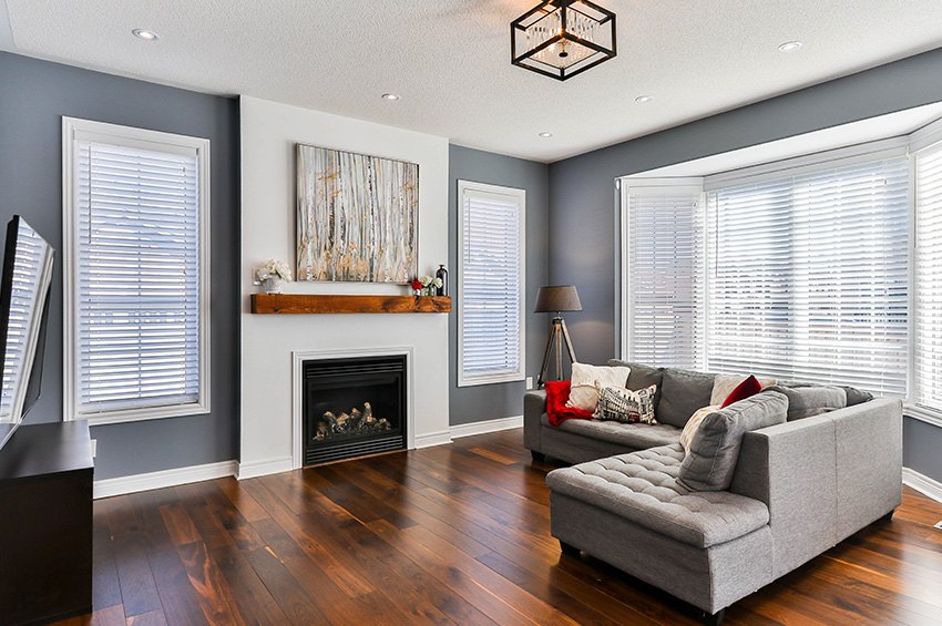 Clean and modern living room features wood-like LVT flooring, gray walls, white brick fireplace with art above the mantle and a grey L-shaped couch.