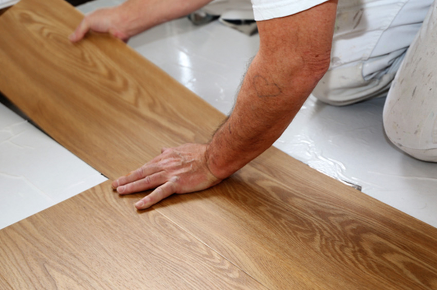 A man works to install remnant LVP flooring in a home.