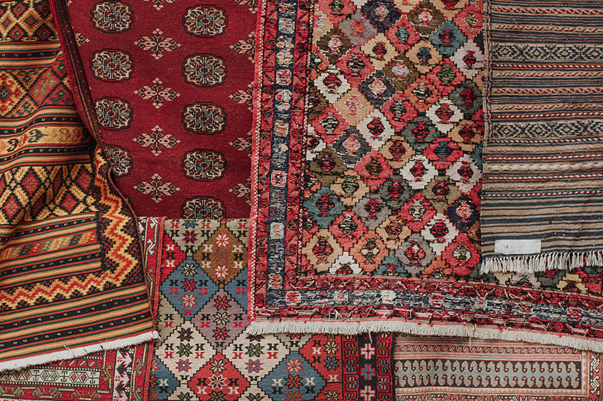 Seven area rugs have been laid on top of each other and all are brightly colored and have different patterns.
