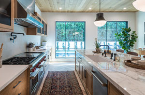 Galley kitchen features rustic wood cabinets, granite countertops, and an area rug with a unique pattern and deep, rich colors.