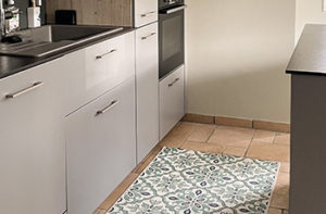 A bright green kitchen area rug with a bold pattern has been placed on stone tiled floors.