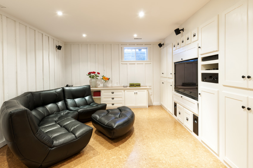 This basement family room includes cork flooring, a comfy black leather couch, and flat screen TV with sound system.