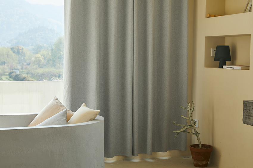 Grey curtains hang in a small living room with gold colored walls and a modern chair.