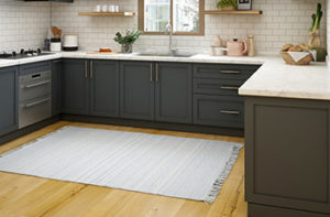 A light grey woven kitchen area rug rests on oak hardwood flooring which complements the kitchen's grey cabinets and subway tiled backsplash.