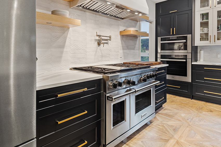 This ultra-modern kitchen features custom designed hardwood flooring, stainless steel appliances, dark grey cabinets with wood pulls, and a gas range and hood.