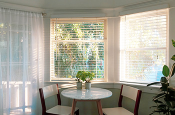 White horizontal blinds let in lots of light into this small kitchen nook that includes a round table and two chairs.