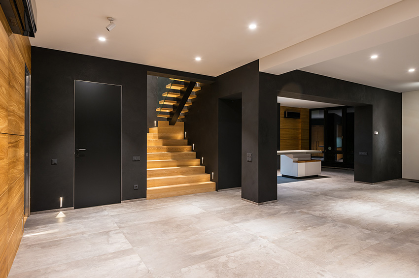 Contemporary basement design features polished concrete flooring, black walls, and floating staircase made from hardwood flooring.