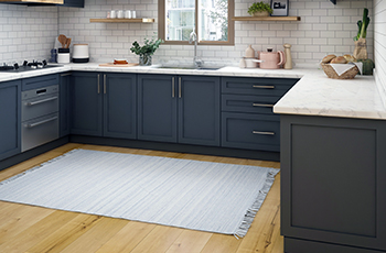 Light blue area rug in a kitchen with dark blue cabinets, white countertops, and subway tile backsplash.