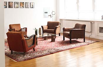 Shiny hardwood floors in a living room that includes an Oriental area rug and comfortable brown chairs.
