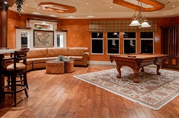 Warm-toned hardwoord floors are in a rec room with a pool table, bar, and couch.