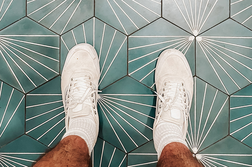 A man in white sneakers is standing on hexagon-shaped green flooring tiles.