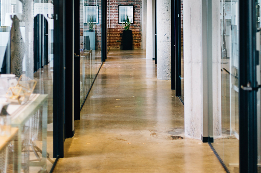 Warm-tone polished concrete floors are in the hallway of a modern office building.