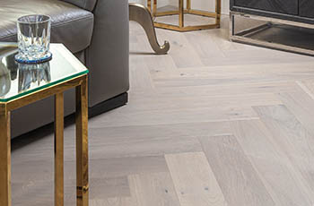 Close up of grey, luxury vinyl plank flooring in a chevron pattern.