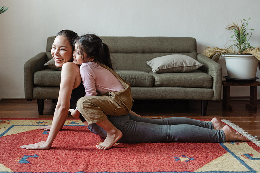 A woman does yoga on a red and gold area rug with her young daughter.