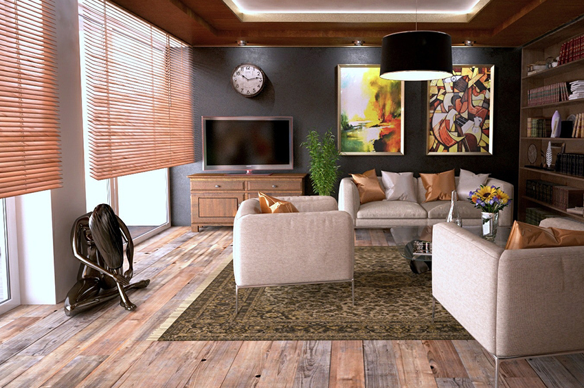 A contemporary living room with area rug has beige furniture, colorful wall art, and rustic hardwood floors.