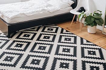 Black and white area rug with geometric pattern in a bedroom with light colored hardwood floors.