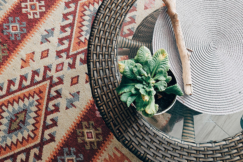 An area rug with a colorful print and unique design sits under a rattan side table.
