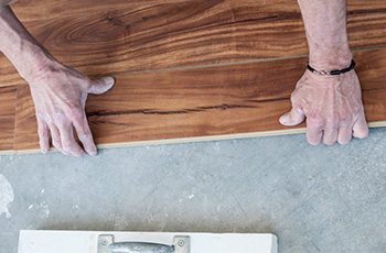 Man installing hardwood flooring over concrete basement floors.