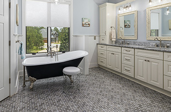 Country farmhouse style bathroom with white clawfoot tub, grey ceramic tile floors, cream cabinets, and quartz countertop.