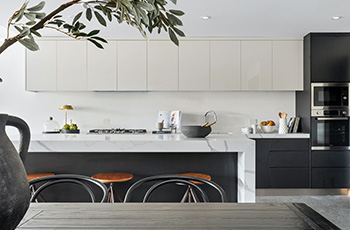 Contemporary kitchen design with white cabinets, white granite countertops, gray vinyl tile flooring, and black appliances.