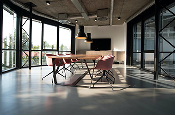 Large office conference room has polished concrete flooring, large floor-to-ceiling windows and industrial style light fixtures.