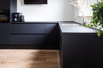This modern kitchen showcases LVP wood-look flooring and dark, sleek, navy blue cabinets.