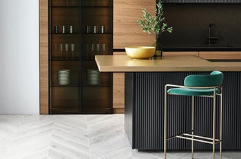 Gray, LVP chevron floors highlight this kitchen design that also includes a wood countertop and retro-blue stool.