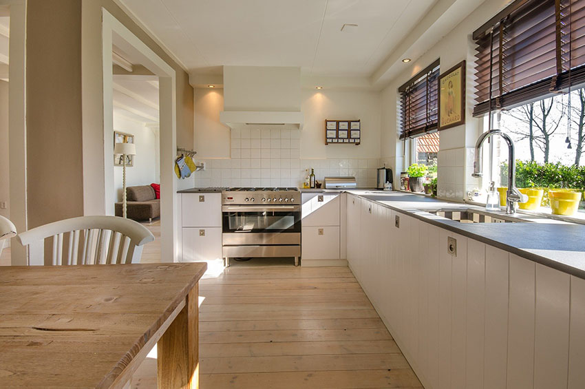 New window blinds in a farmhouse-style kitchen with rustic wood floors, white cabinets, and granite countertop.