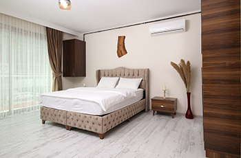 Bedroom with a quilted beige bed frame and extremely light wood look tile flooring.