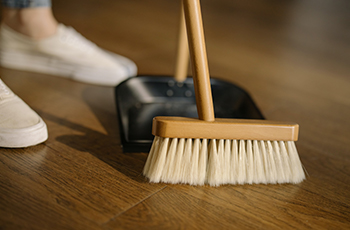 Close up of a person in white sneakers sweeping a wood floor.