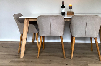 Dining room close up shot with medium-toned luxury vinyl flooring and a beige dining table and chair set.