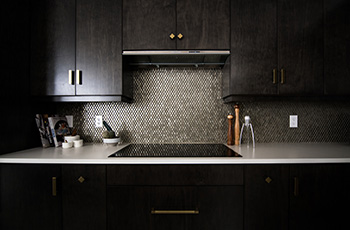 Dark, dramatic kitchen cabinets with a white countertop and beige penny tile backsplash.