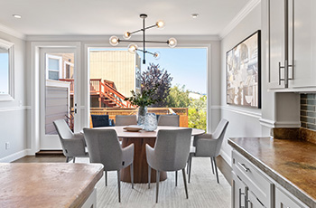 View of dining area with a round table, gray chairs, and a modern light fixture that faces a large picture window.