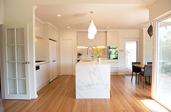 Bright and airy kitchen with light vinyl wood floors, white walls, and a marble island.