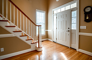 Bungalow front entrance with a stately front door framed by windows, a classic banister, and beautiful light-wood floors.