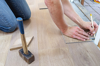 Contractor measuring for wooden floor installation. A mallet is to the left.