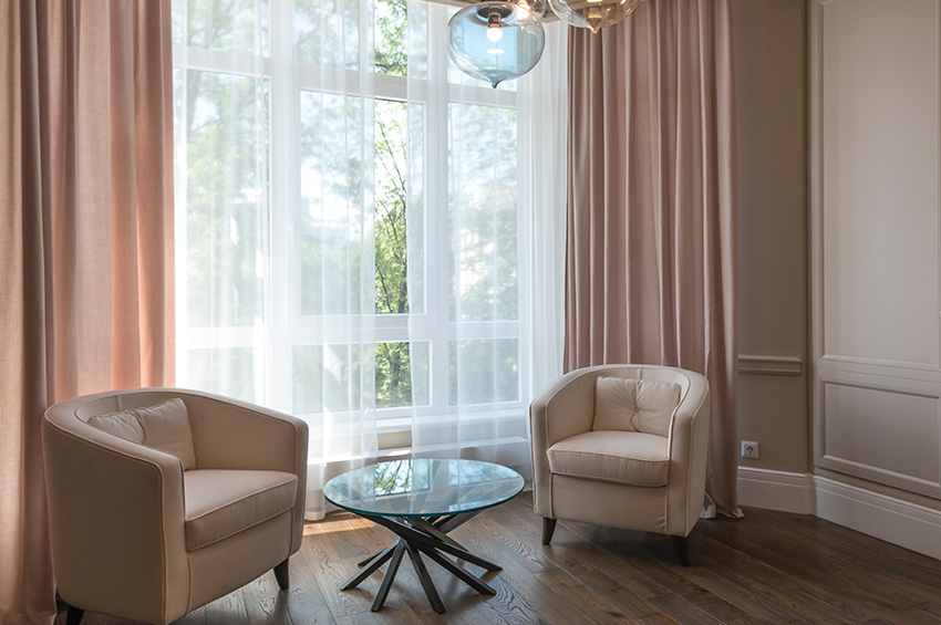 Elegant seating area with two comfortable chairs and a side table next to a large window with pink drapes and dark vinyl flooring.